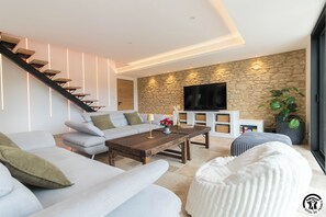 Ein modernes Wohnzimmer mit Treppe, einer Wand aus Steinoptik, einem Flachbildfernseher und einer großen Topfpflanze.