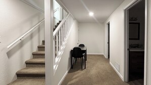 A hallway with carpeted stairs, a dining area with chairs, and a door leading to another room.