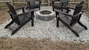 A backyard with a fire pit surrounded by four Adirondack chairs.