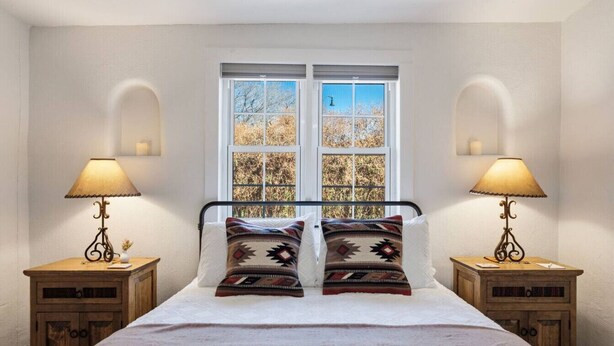 Une chambre à coucher avec un lit, deux tables de chevet avec des lampes, une fenêtre donnant sur des arbres et une literie à motifs.