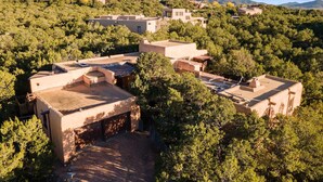 A residential area with multiple buildings surrounded by dense greenery and hills in the background. - Authentic Adobe Retreat - Family & Group Getaway (Santa Fe)