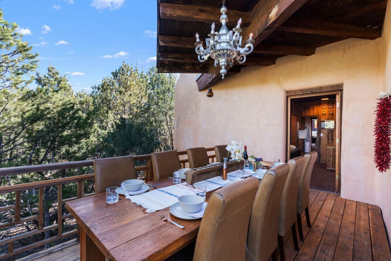 A dining area with a wooden table set for four, surrounded by chairs, and a view of trees in the background.