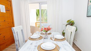 Una mesa de comedor vestida con platos blancos, vasos y un florero con flores, rodeada de individuales tejidos.
