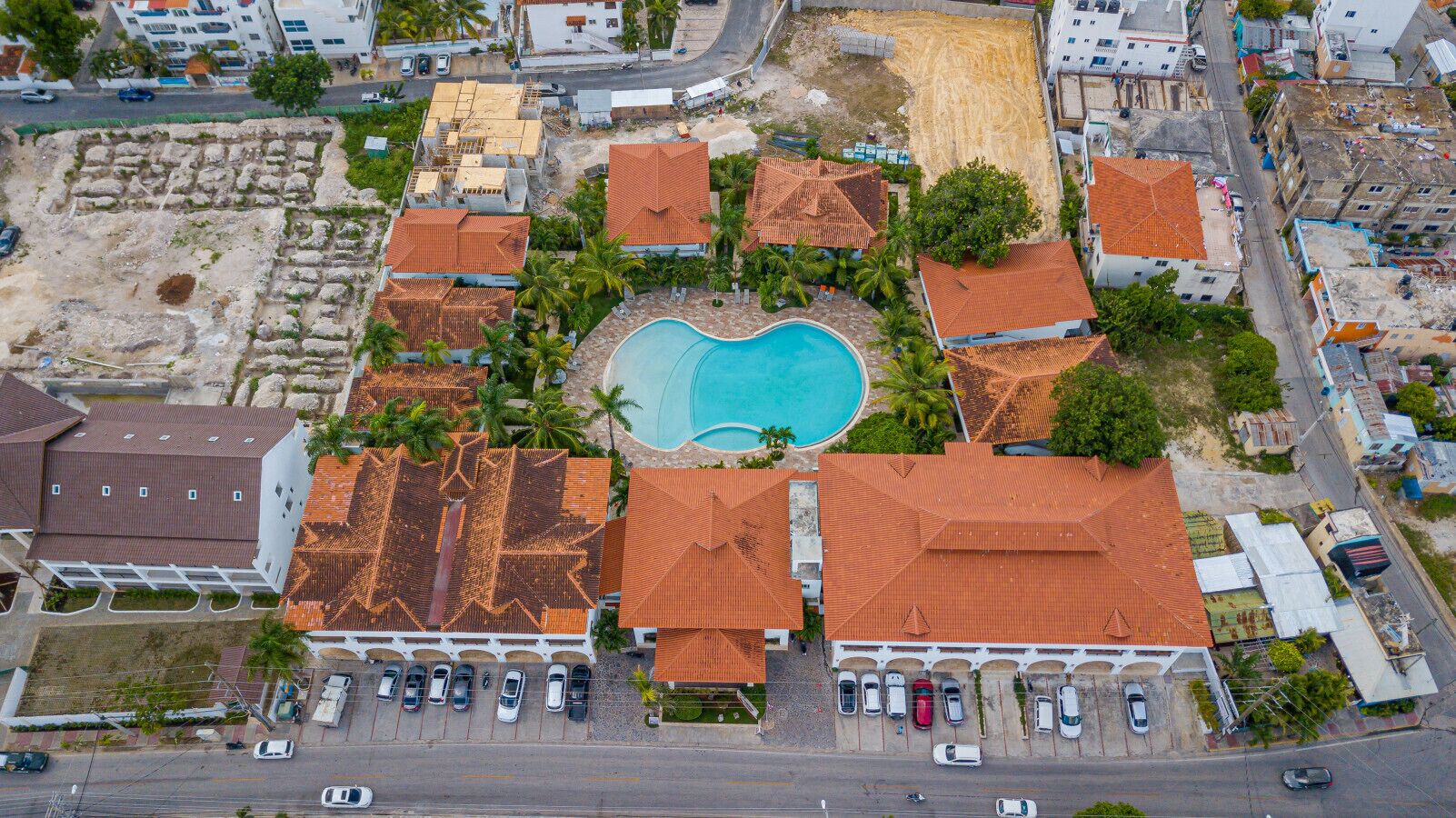 An aerial view of a resort with a swimming pool, multiple buildings with red roofs, and a parking area.