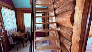 A wooden staircase with a metal railing in a room with a dining area and a purple wall. - Cabaña 1 Hogar de leña puente colgante (Mineral del chico)