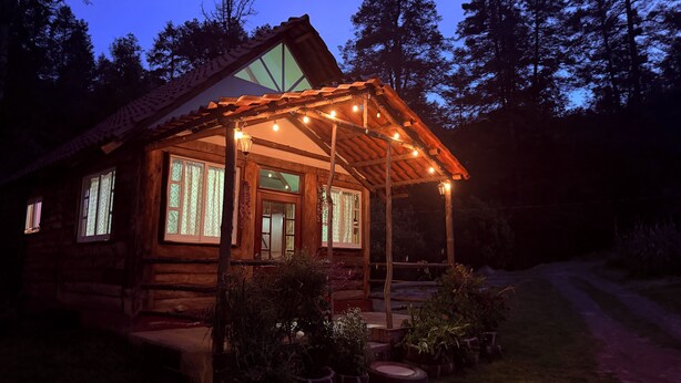A log cabin with a covered porch, large windows, and potted plants. - Cabaña 1 Hogar de leña puente colgante (Mineral del chico)