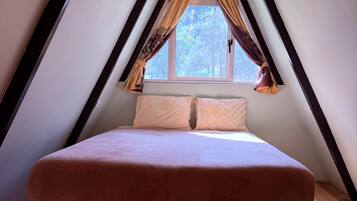 Ein Schlafzimmer mit Bett in einem giebelartigen Dachraum, Holzboden und einem fenster mit Vorhängen.