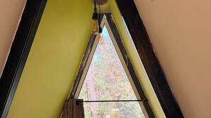 Una habitación con techo inclinado, una ventana con cortinas y vista a árboles.