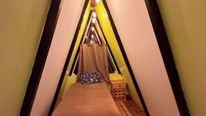 Una habitación acogedora y triangular con una cama en el centro, suelo de madera y un pequeño cofre de madera.