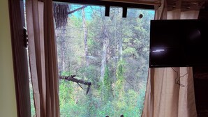 A room with a large window, wooden floor, and a bed with a patterned cover.