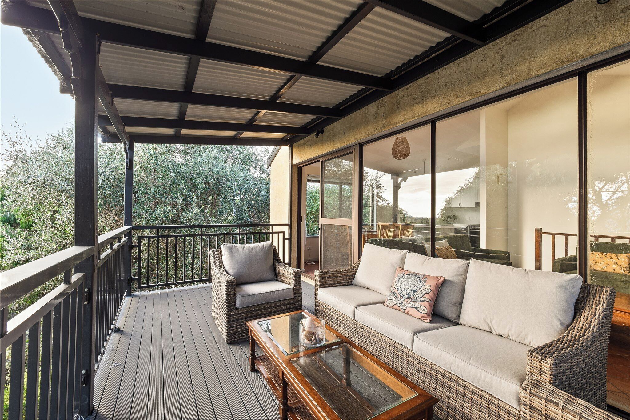 A covered outdoor seating area with wicker furniture and a glass table.