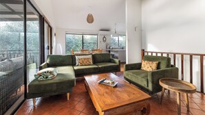 Ampla sala de estar com sofá verde, mesa de centro de madeira e varanda com vista.