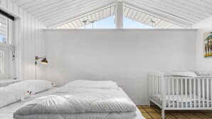 Quarto com decoração em tons de branco, uma cama grande, berço e claraboia.