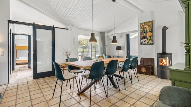 Uma ampla área de jantar com mesa de madeira e cadeiras modernas, uma janela grande com vista e uma parede verde decorativa.