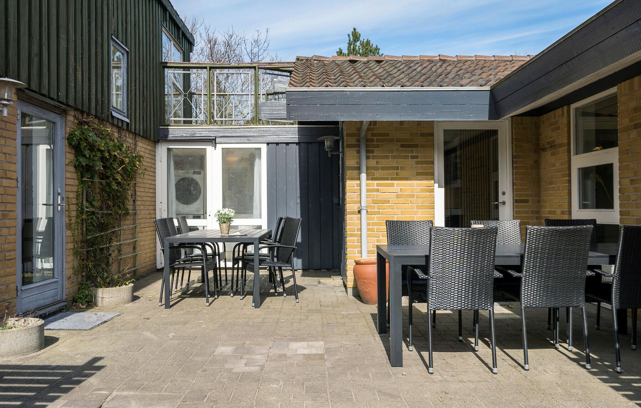A patio with two tables and chairs, a brick wall, and a window.