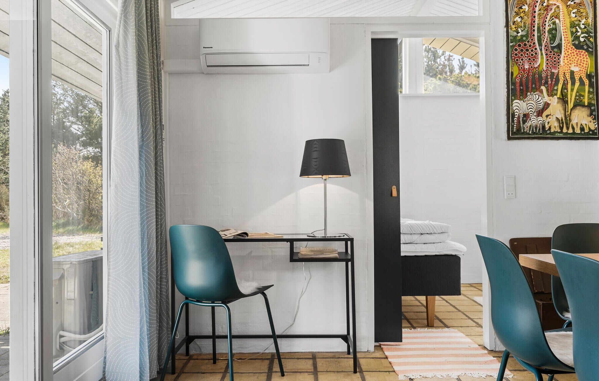 A modern room with a desk, chairs, a lamp, and a painting on the wall.