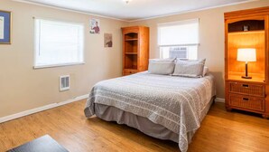 A bedroom with a bed, a nightstand, a wooden wardrobe, and a window with blinds. - Family & Dog Oasis (Knoxville)