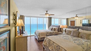 Een hotelkamer met twee bedden, een groot raam met uitzicht op de oceaan, plafondventilatoren en een houten vloer.
