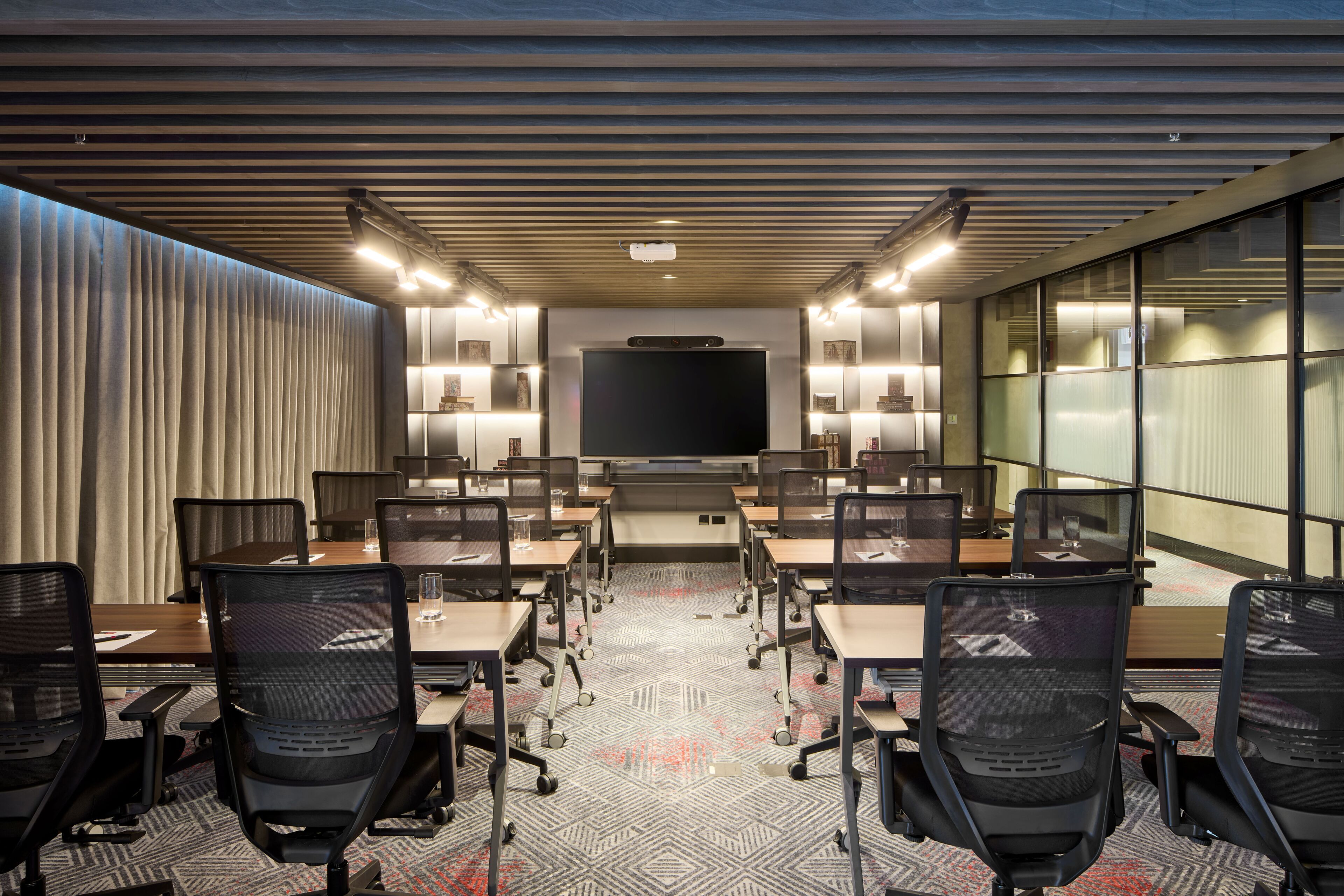 A conference room with a large flat-screen TV, multiple tables, chairs, and a patterned carpet.