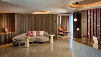 A modern lobby with a curved reception desk, a sofa with red and white cushions, and a small side table with a vase.
