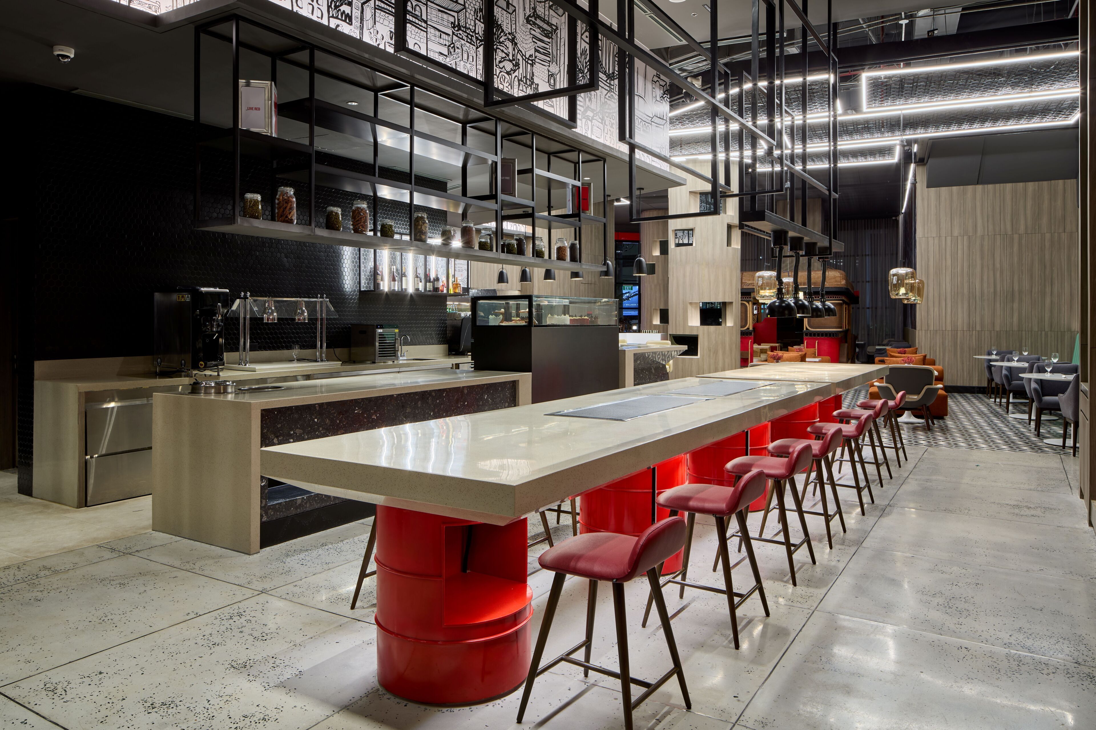 A modern bar area with a long counter, red stools, and a high ceiling with exposed beams.