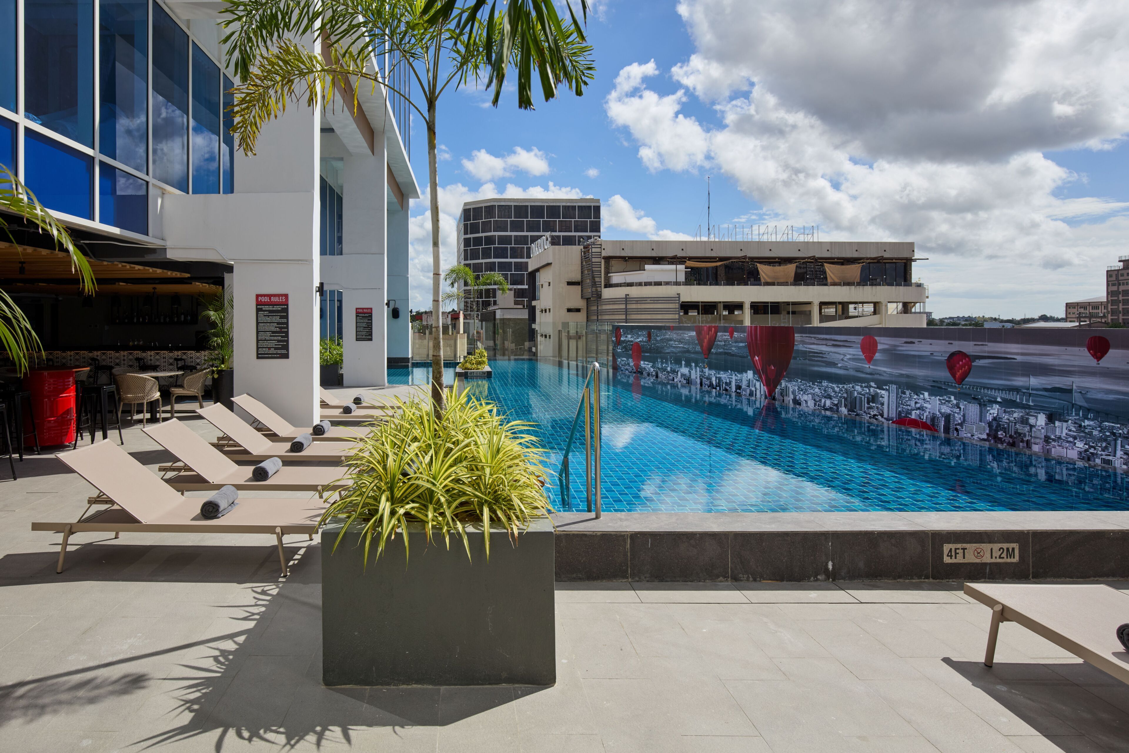 A rooftop pool with sun loungers, a bar area, and modern buildings in the background.