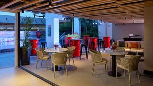 An indoor dining area with wicker chairs, round tables, red barrels, and potted plants. - Radisson RED Cebu Mandaue (Mandaue)