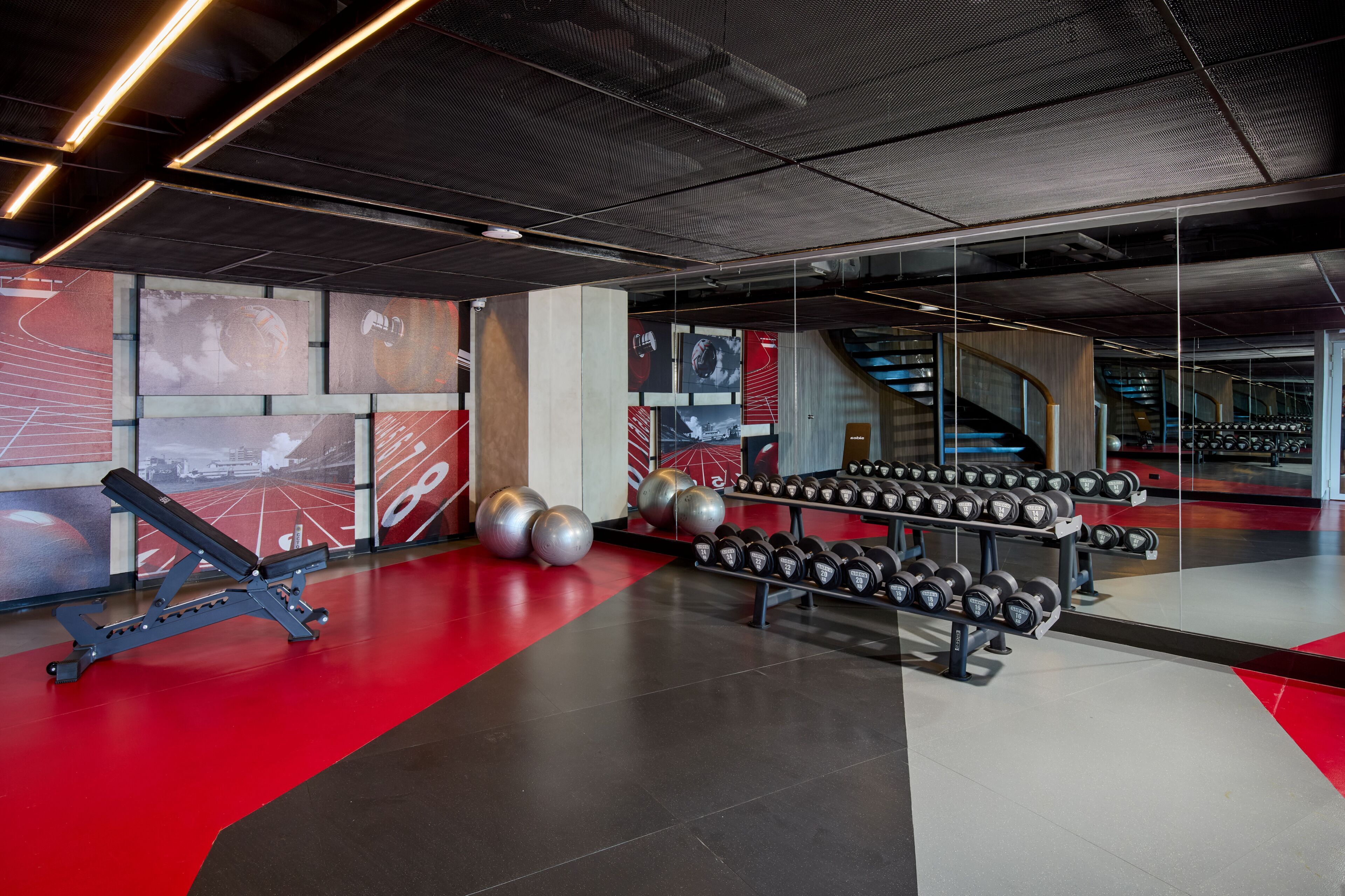 Un gimnasio con equipo de ejercicio, piso rojo y pared espejada.