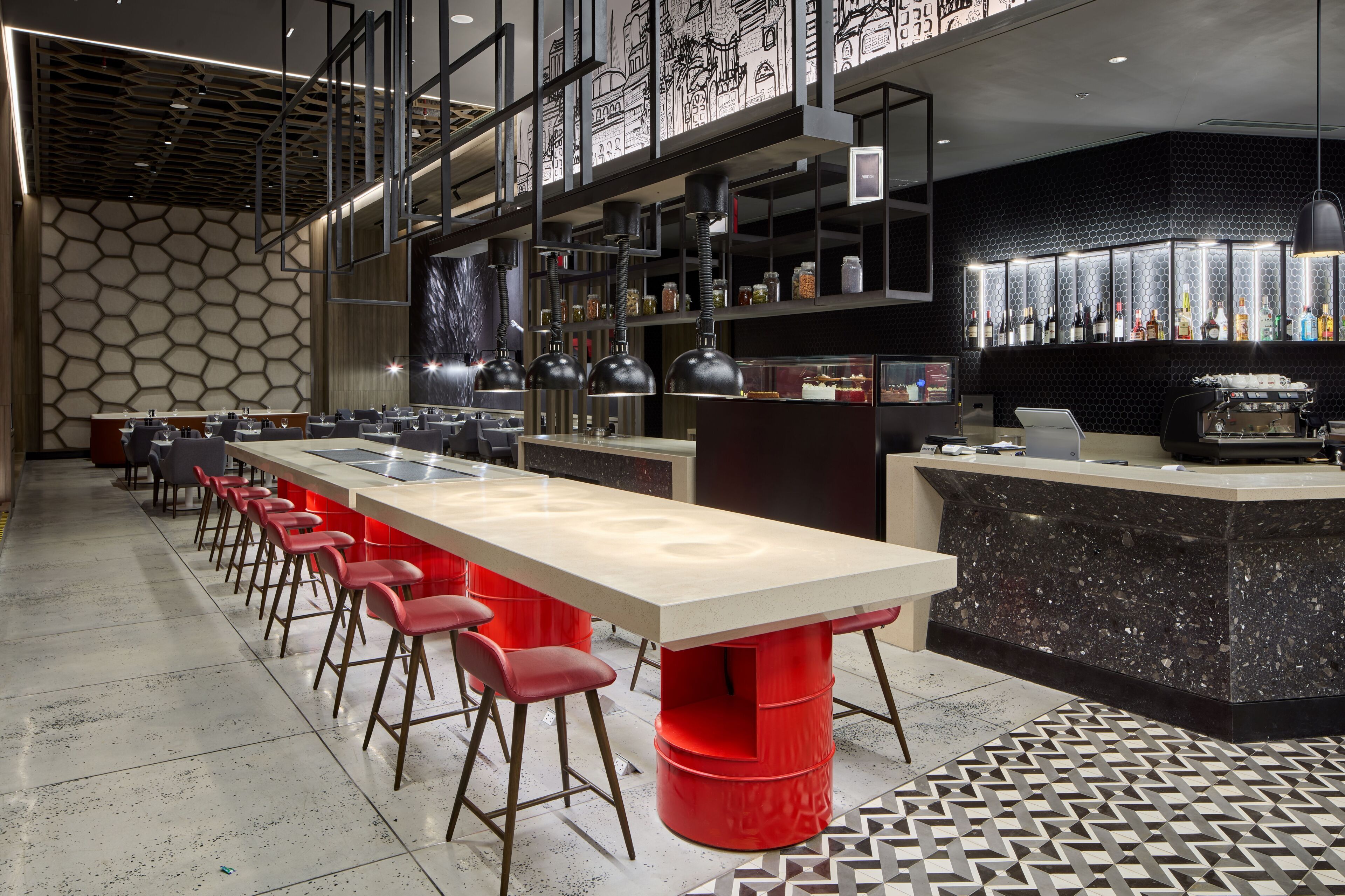 Zona de bar moderna con una barra larga, taburetes rojos y una exhibición de botellas.