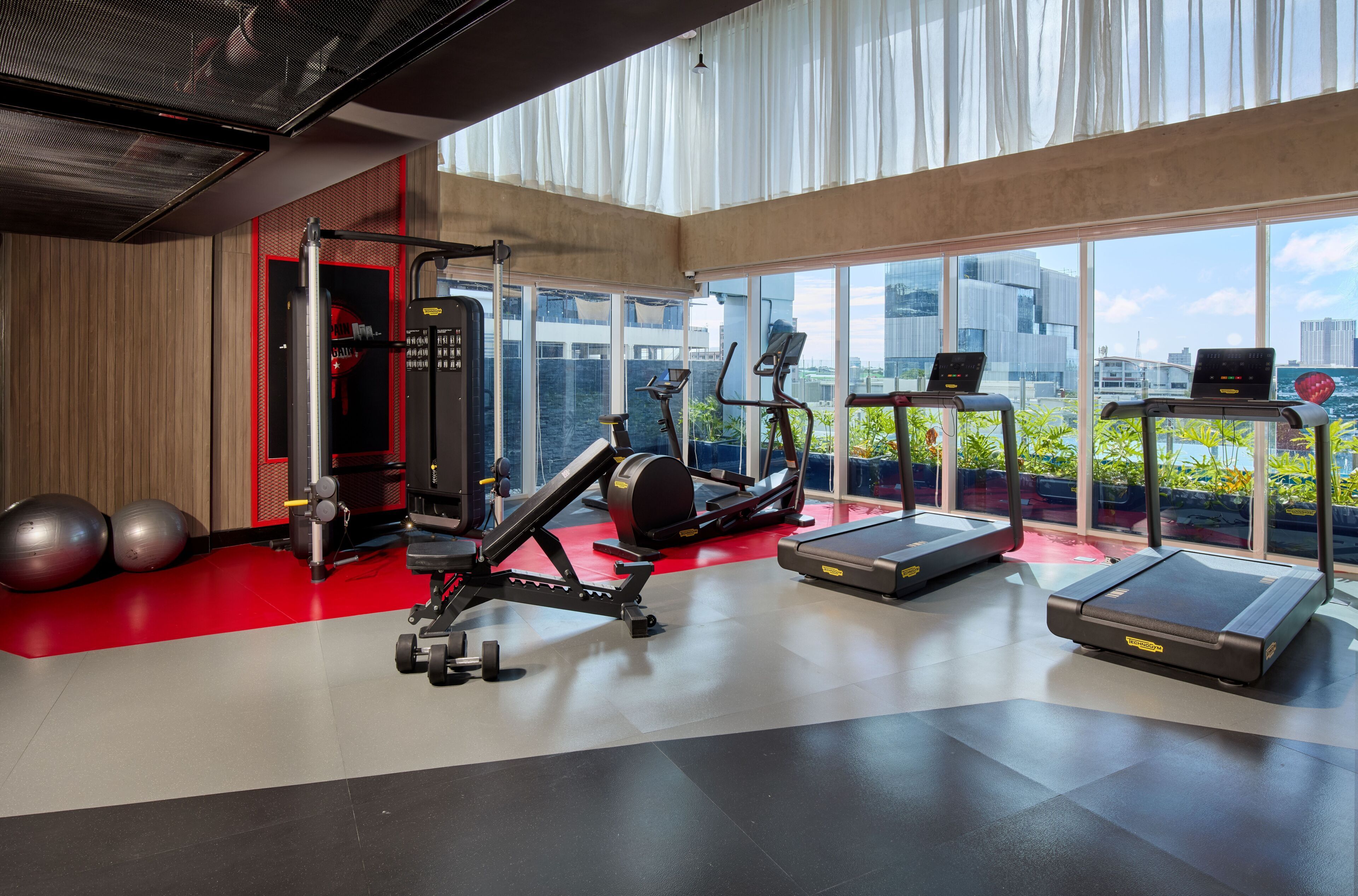 Une salle de sport équipée de matériel d’exercice, dotée de grandes fenêtres et offrant une vue sur la ville.