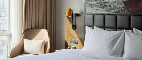 Habitación de hotel con cama, una silla, una lámpara de pared y un ventanal grande.