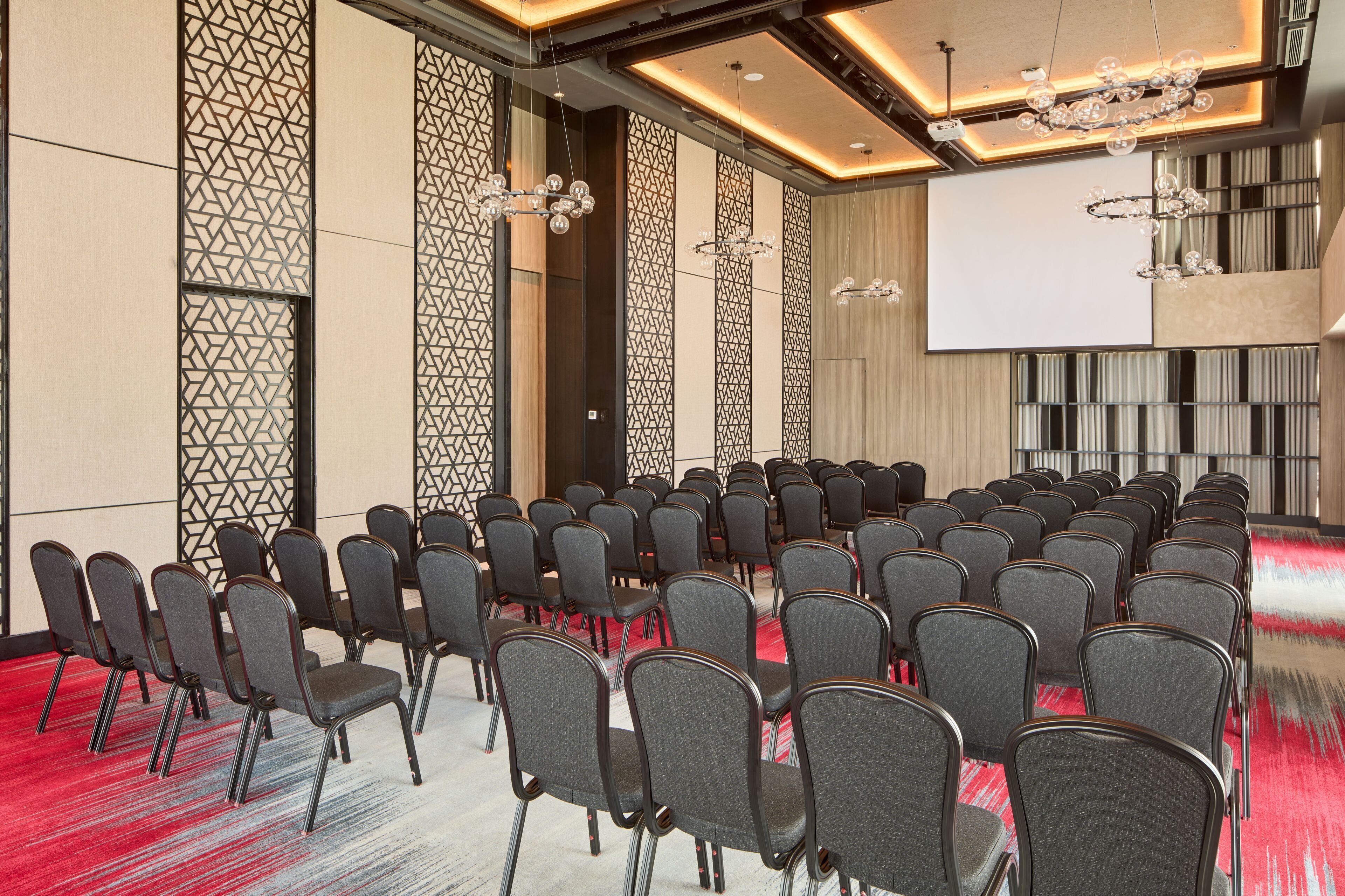 A conference room with rows of chairs, a large screen, and decorative lighting fixtures.