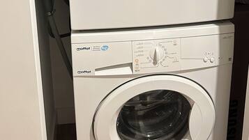 Un appareil combiné lave-linge et sèche-linge, de type « empilable », doté de panneaux de commande et de tuyaux.