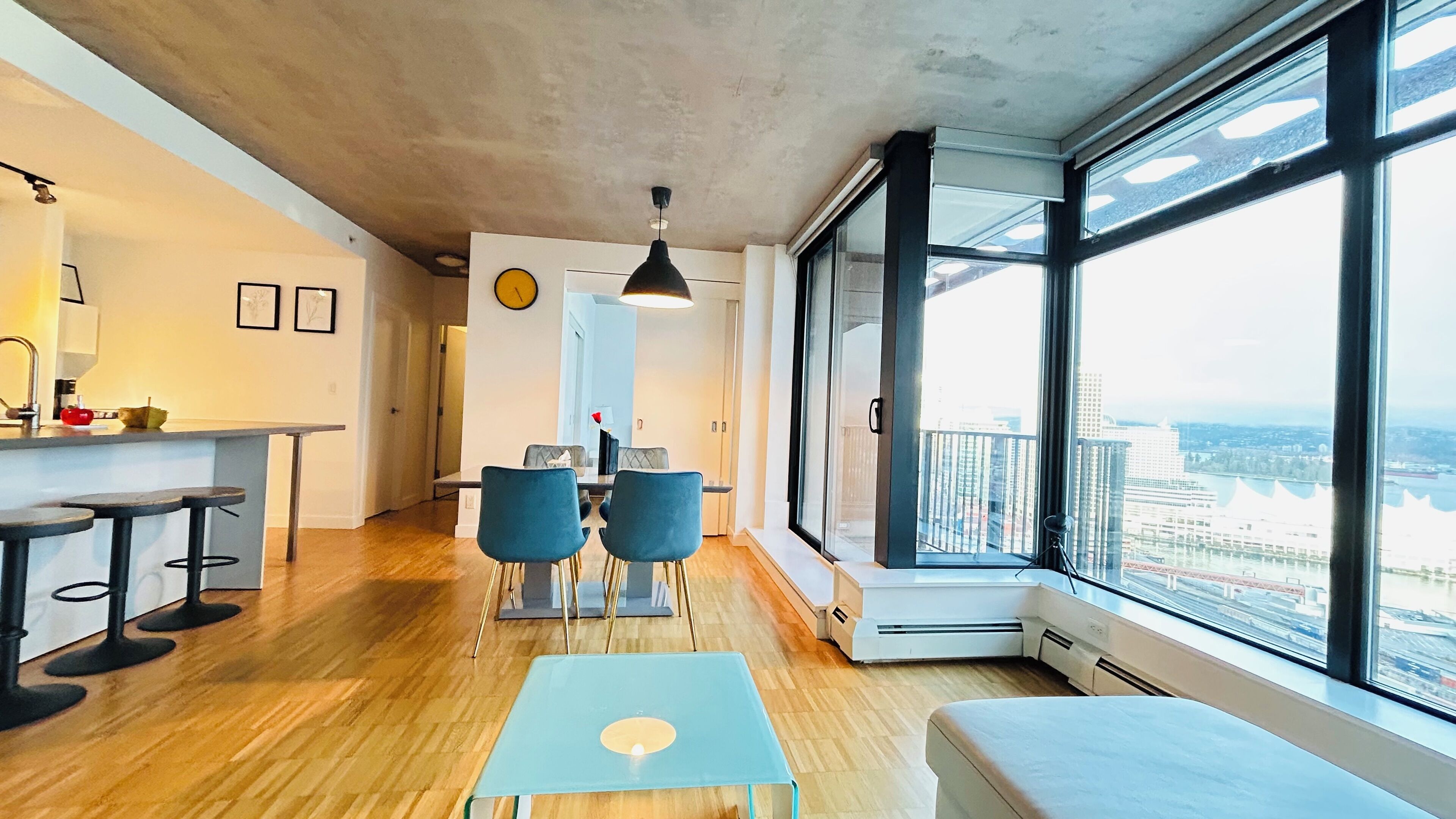 A modern apartment with a dining area, a kitchen, and large windows offering a city view.