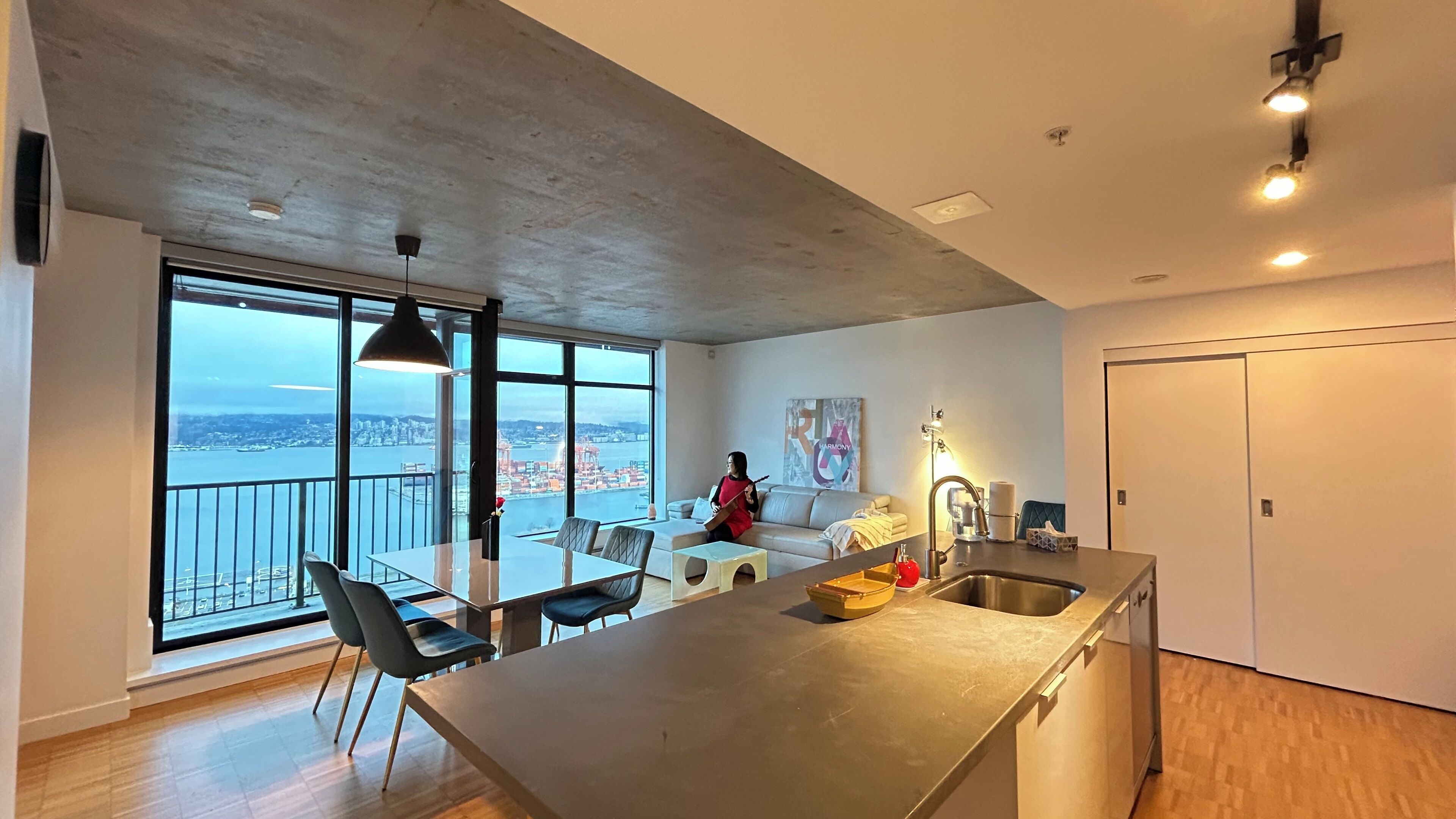 A modern kitchen with a large island, a dining area with a glass table, and a view of a cityscape through large windows.