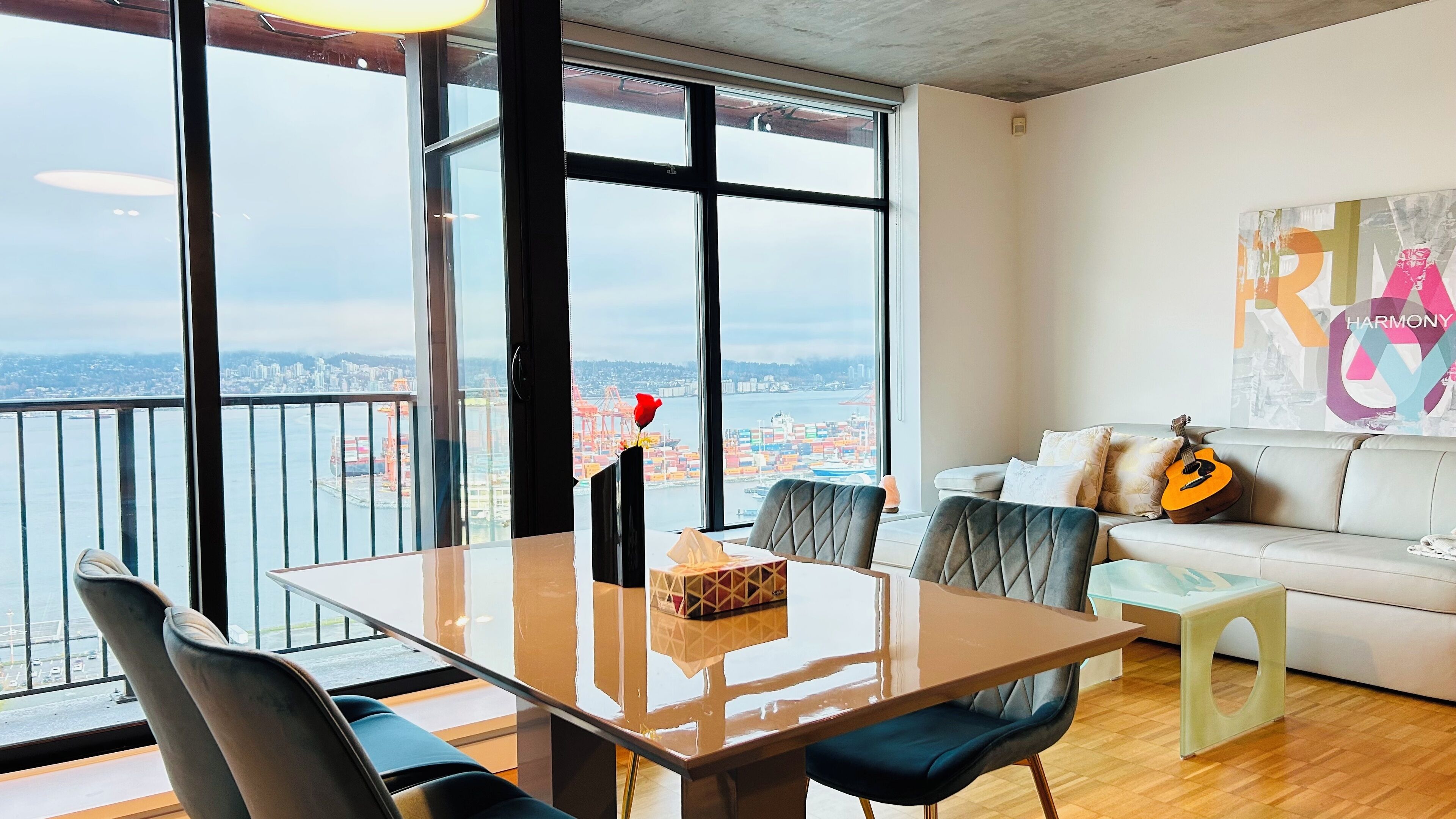 A modern living room with a large window overlooking a cityscape, a dining table with chairs, a sofa, and a guitar.