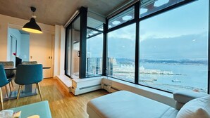 A modern hotel room with a large window offering a view of a waterfront and cityscape.