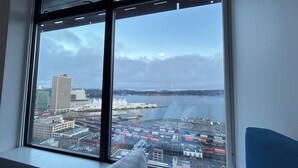 A cityscape through a window with a view of buildings, a body of water, and a cloudy sky.