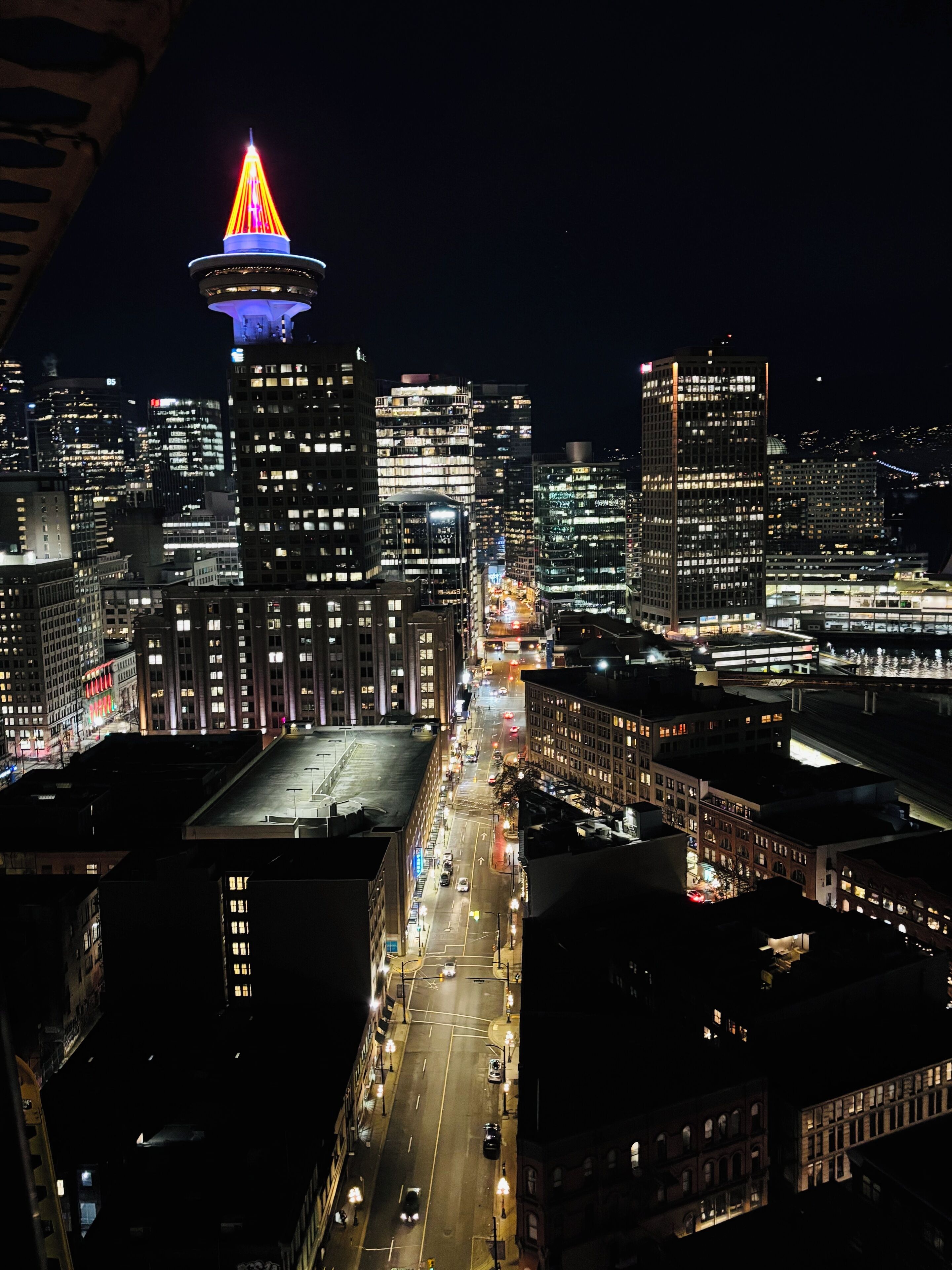 A nighttime cityscape with illuminated buildings and a prominent tower with a colorful spire.