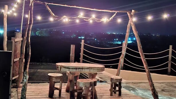 Un espace extérieur aménagé avec des meubles en bois rustique et des guirlandes lumineuses, offrant une vue sur le paysage urbain illuminé la nuit.