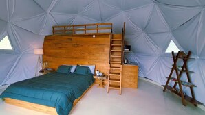Un dormitori tipus tenda acollidor amb un llit doble de fusta, una taula de nit petita i una escala.