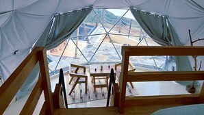 Una tenda acollidora amb sòl de fusta, un llit i una taula amb cadires.