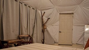 Une pièce aménagée avec une tente, un lit, une chaise en bois, une porte et un objet fixé au mur.