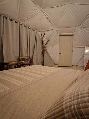 Una habitación con carpa, una cama, una silla de madera, una puerta y un objeto fijado a la pared.
