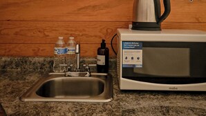 Une cuisine équipée d’un évier en acier inoxydable, d’un four à micro-ondes, d’une bouilloire et d’une étagère où sont rangés des verres à vin et une bouteille.