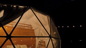 Une tente en forme de dôme géodésique, équipée d’un lit, de meubles en bois et d’une échelle.