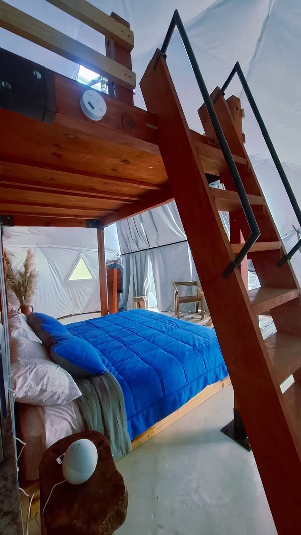 A tent with a bed, a ladder, and a small table.
