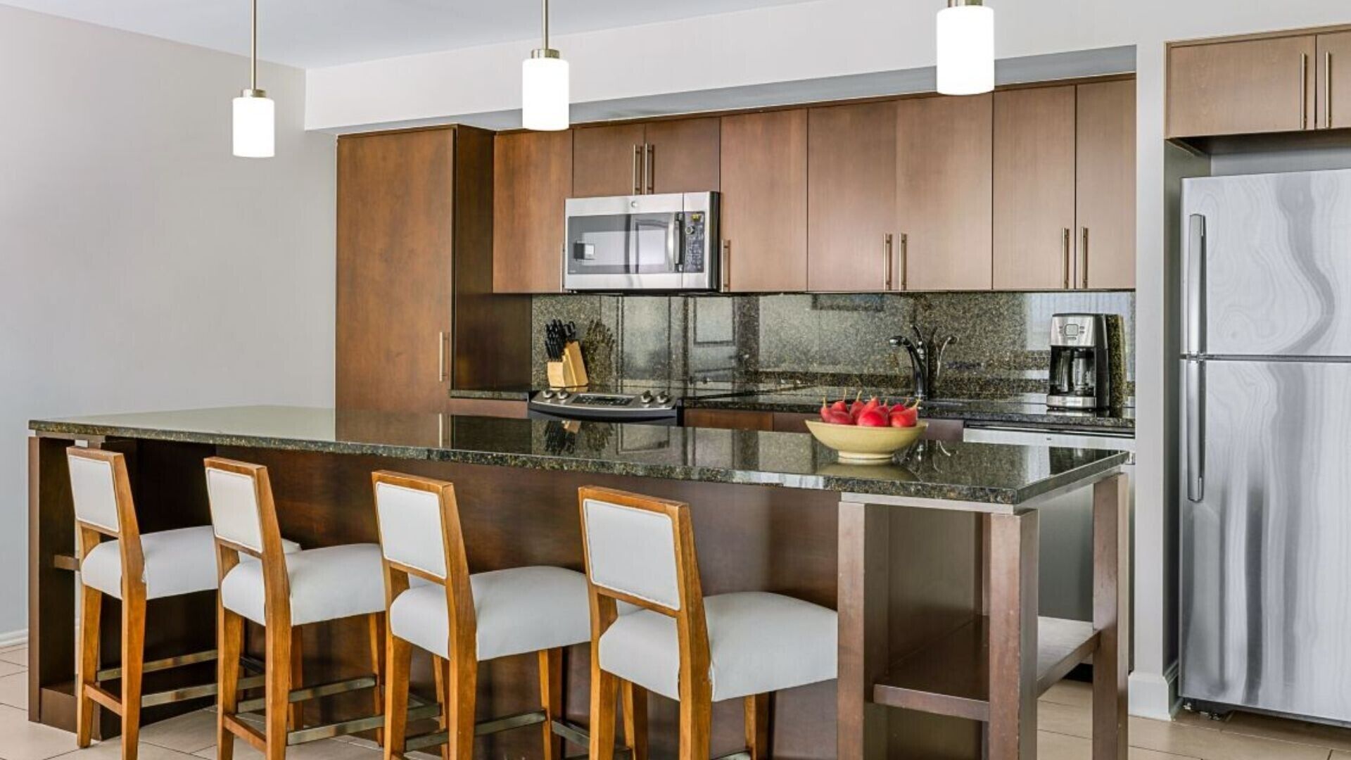 A modern kitchen with a central island, bar stools, stainless steel appliances, and a granite countertop.