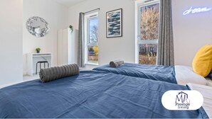 A modern bedroom with two beds, a large window, a clock, and a neon sign. - Central Home | Fast Wi-Fi | Smart TVs | Sleeps 5 (Birmingham)