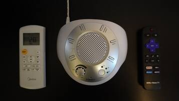 A white bedside table with a digital clock, a white bedside speaker, and a black remote control.
